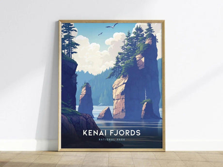 Framed poster of Kenai Fjords National Park featuring towering rock formations, lush trees, and serene water under a cloudy sky, leaning against a white wall on a wooden floor.