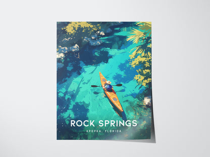A vibrant poster depicts a kayaker in an orange kayak navigating clear blue waters surrounded by lush greenery. The text reads Rock Springs, Apopka, Florida.