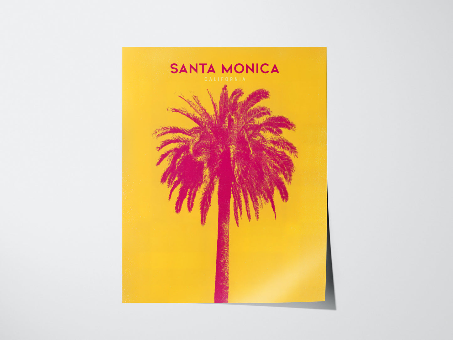 A vibrant poster featuring a pink palm tree against a bright yellow background with the text Santa Monica, California at the top. The design is bold and eye-catching.