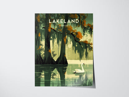 Illustrated poster featuring a serene lake scene with a swan gliding across water, surrounded by moss-covered trees and autumn foliage, titled Lakeland Florida. The reflection enhances the tranquil atmosphere.