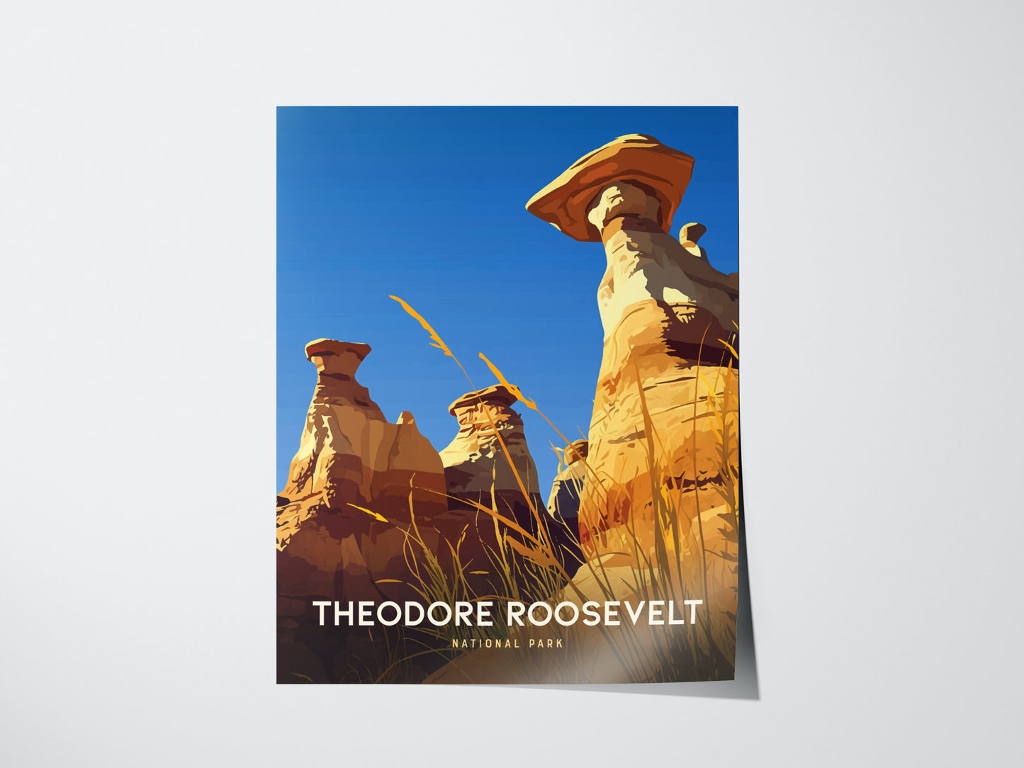 The image shows a poster of Theodore Roosevelt National Park featuring striking hoodoos under a clear blue sky, with tall grasses in the foreground.