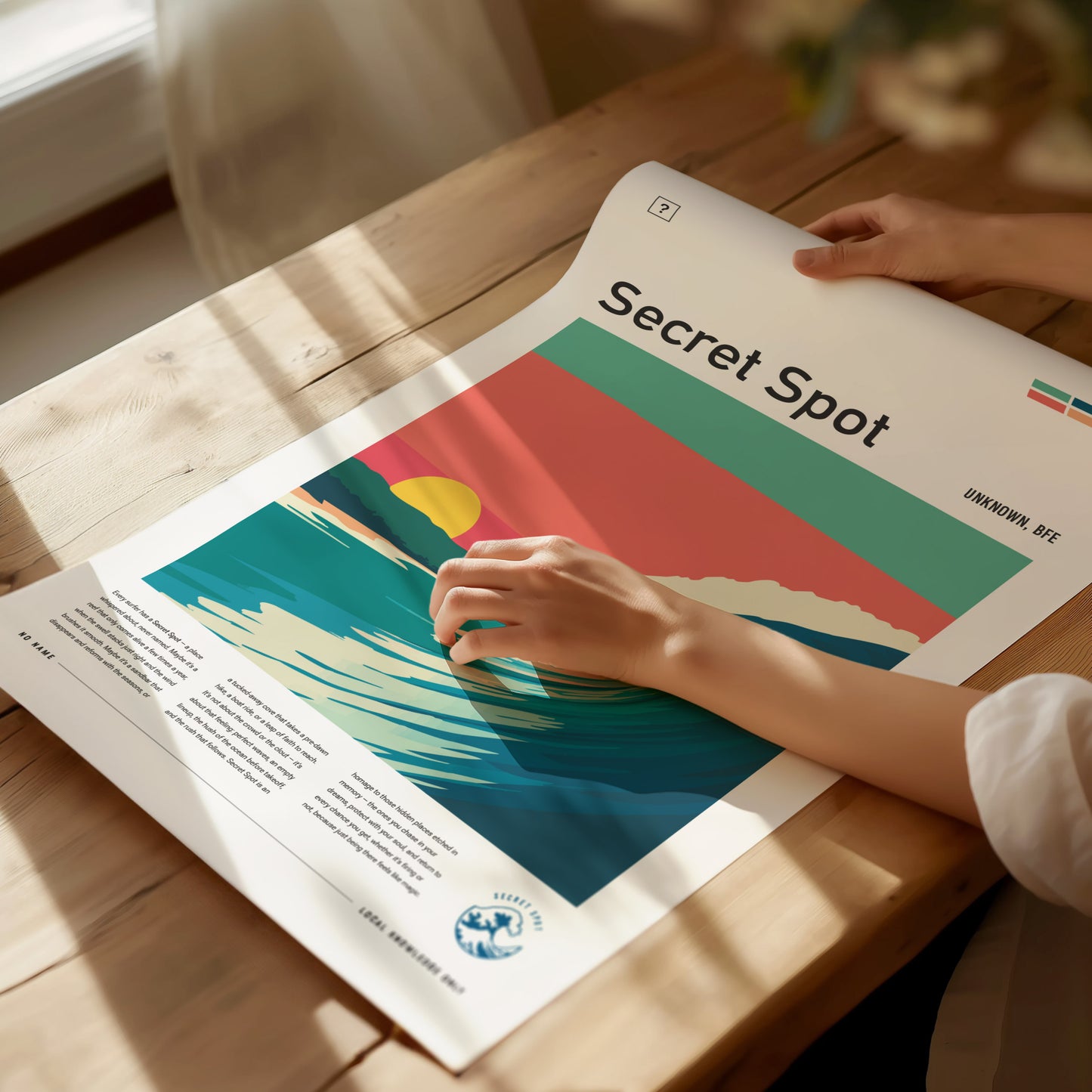 A person gently holds a colorful surf poster titled Secret Spot on a wooden table, with soft sunlight illuminating the scene.