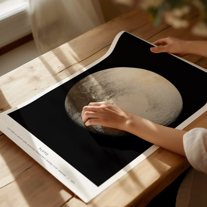 Person holding a poster with an image of Pluto, on a wooden table.