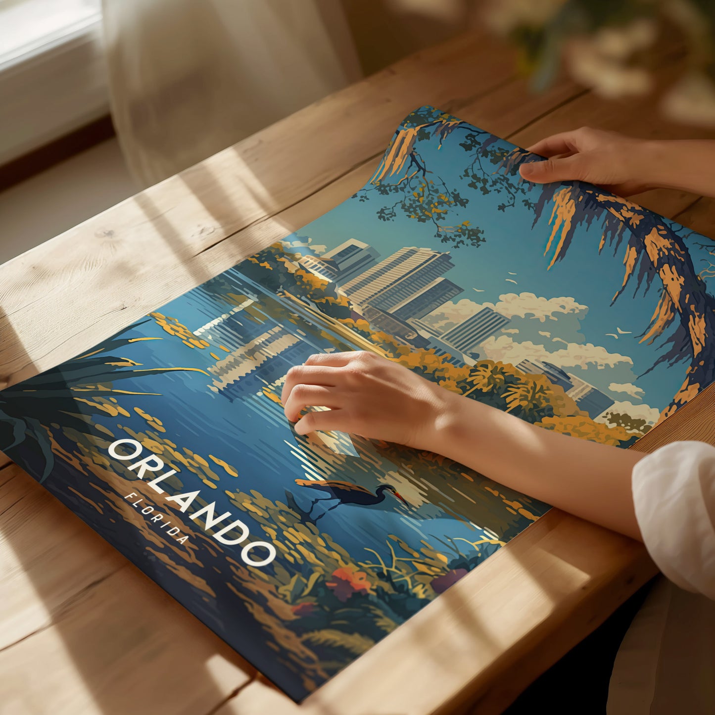 A person rolls out an Orlando poster featuring a stylized downtown skyline, Lake Eola, and a bird on a wooden table. Sunlight casts soft shadows across the scene.