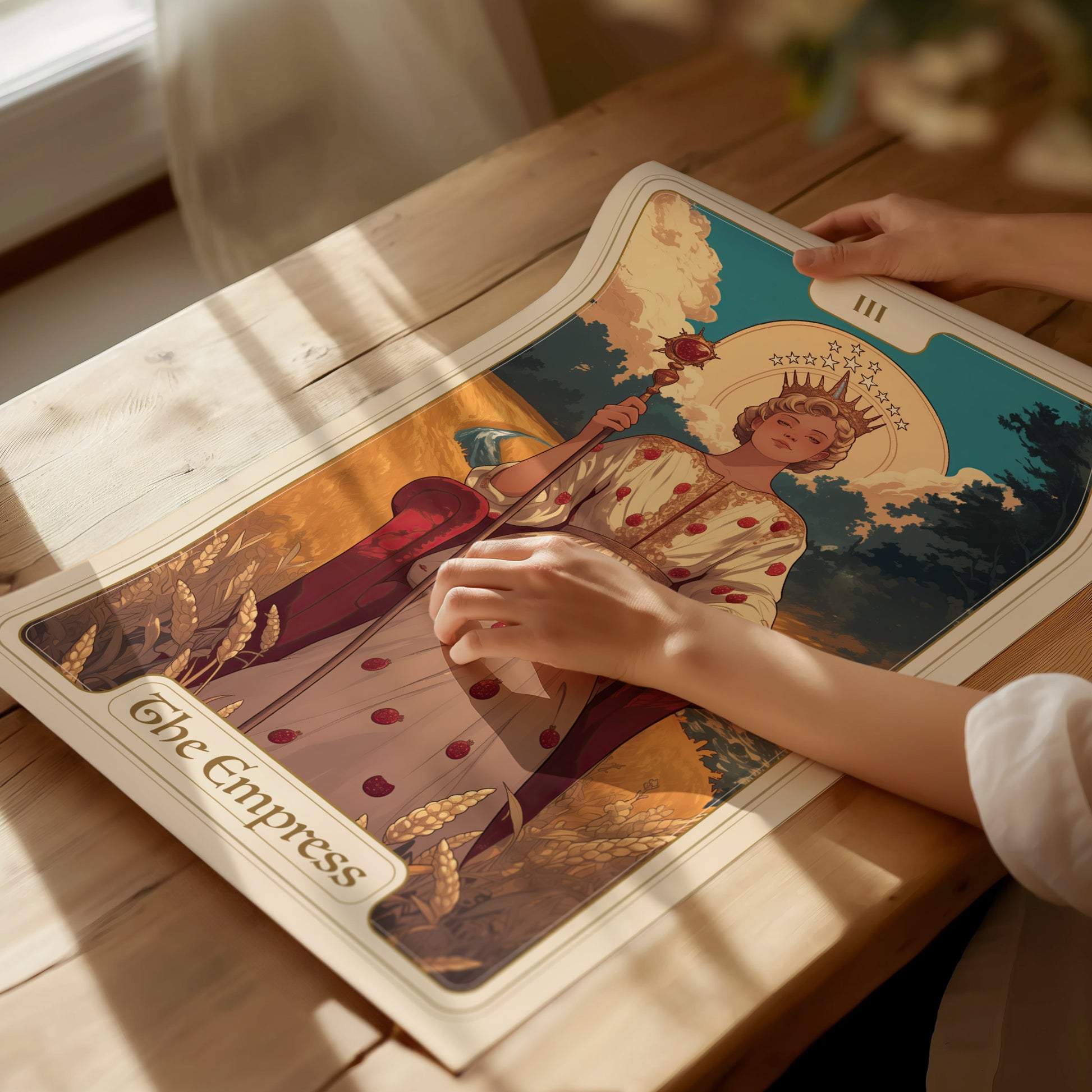 A person gently unrolls an Empress Tarot poster on a wooden table, featuring a regal figure with a crown and wheat motifs, surrounded by warm sunlight.