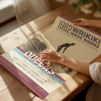 A person adjusts a vintage 1962 Waikiki Wave Riders surfing competition poster on a wooden table. The poster features retro typography and an image of a surfer.