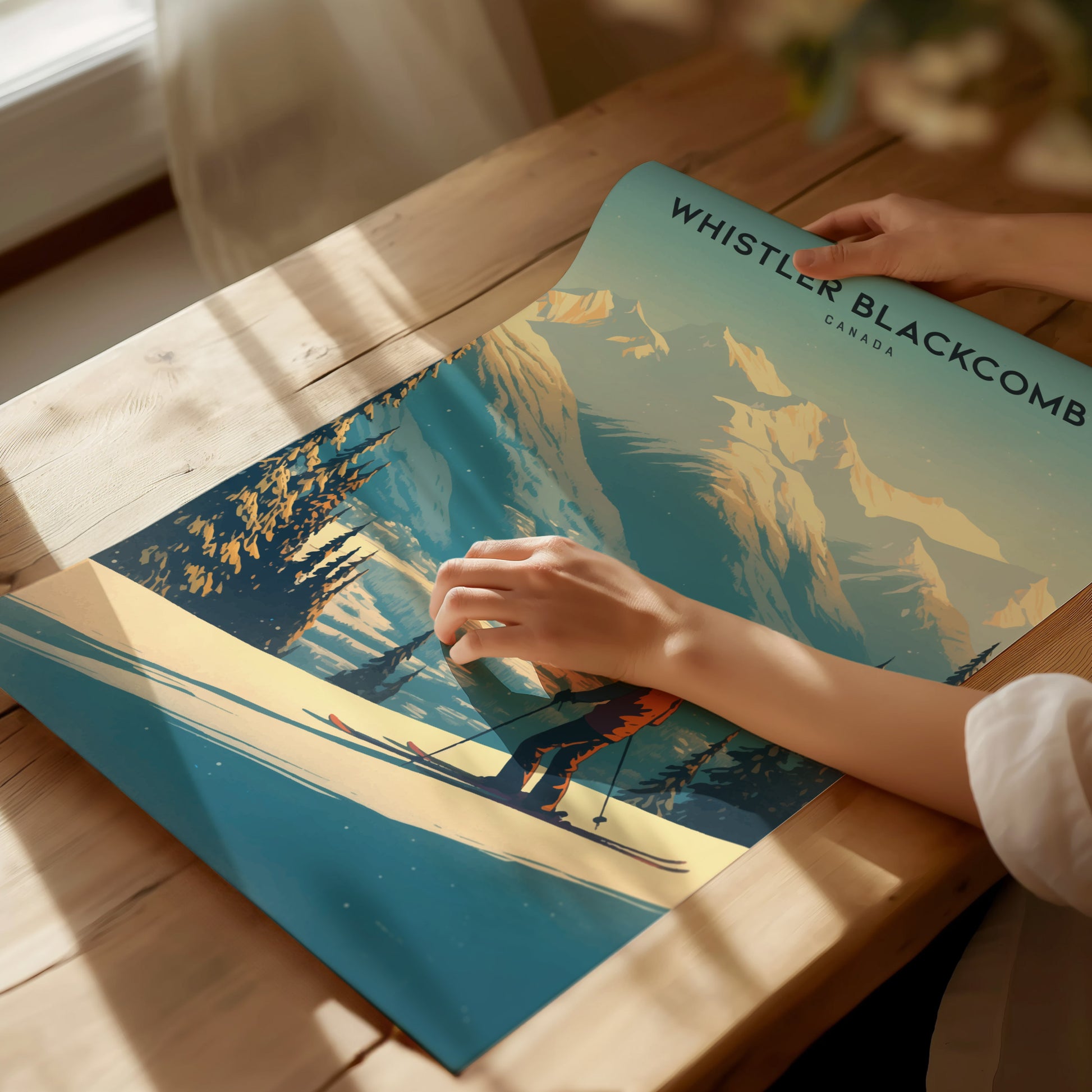 A person holds a Whistler Blackcomb poster depicting a skier on snow-covered slopes with scenic mountains in the background, placed on a sunlit wooden table.