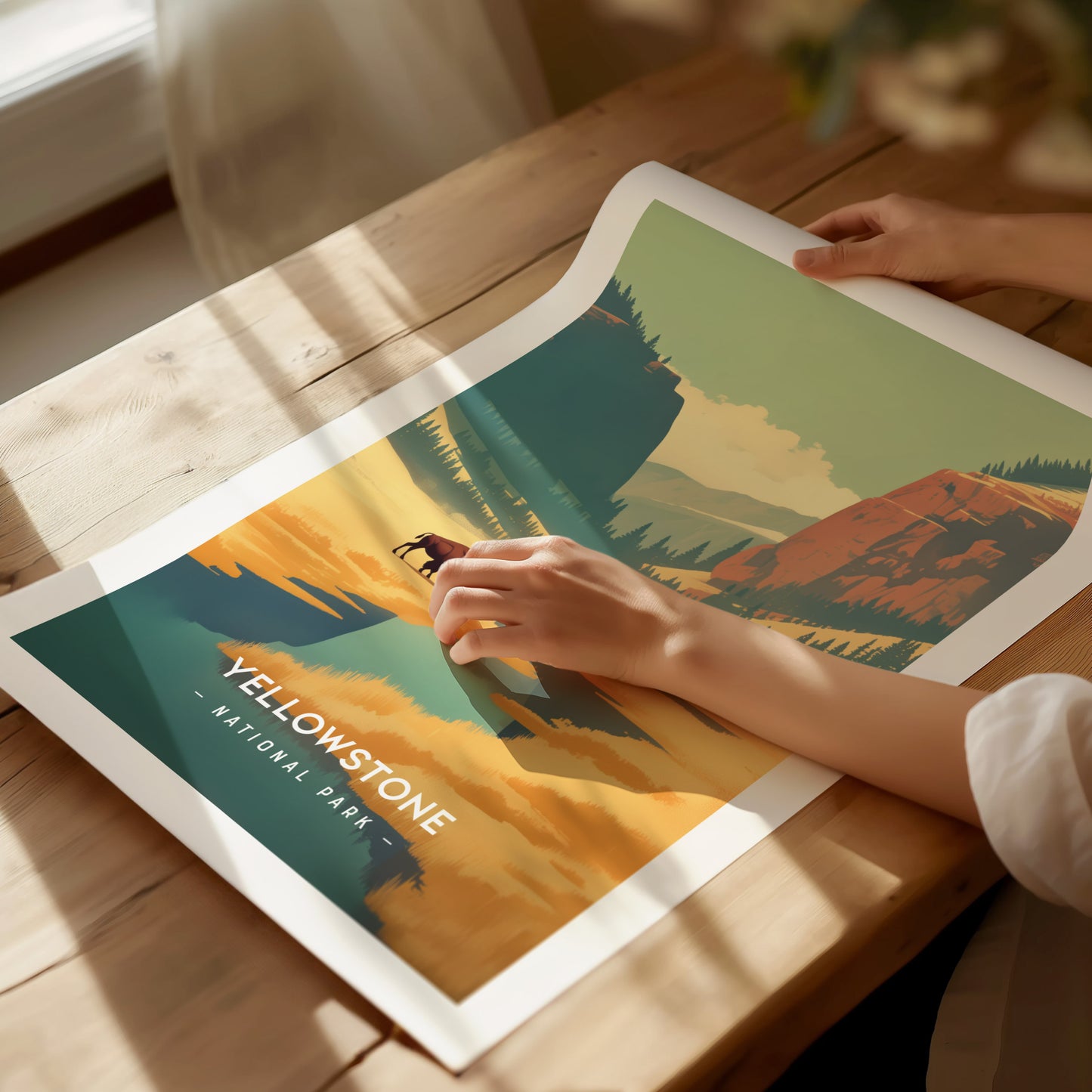 A person is holding a colorful poster of Yellowstone National Park on a wooden table, featuring bold graphics of mountains.