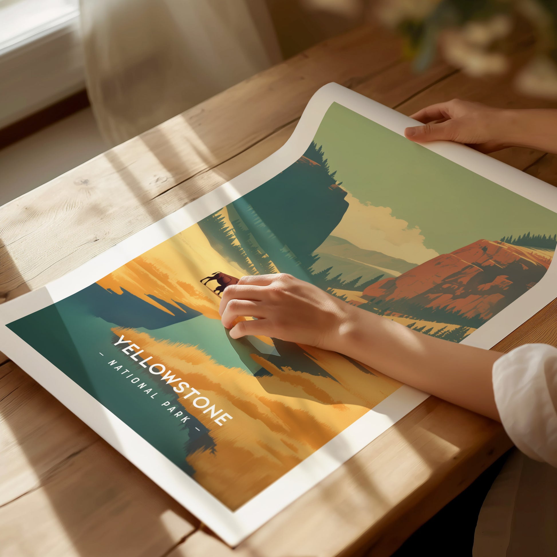 A person is holding a colorful poster of Yellowstone National Park on a wooden table, featuring bold graphics of mountains.
