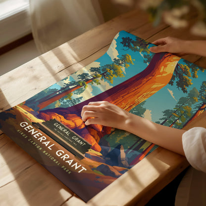 A person adjusts a colorful poster of the General Grant Tree on a wooden table, depicting a vibrant giant sequoia in Kings Canyon National Park under soft.