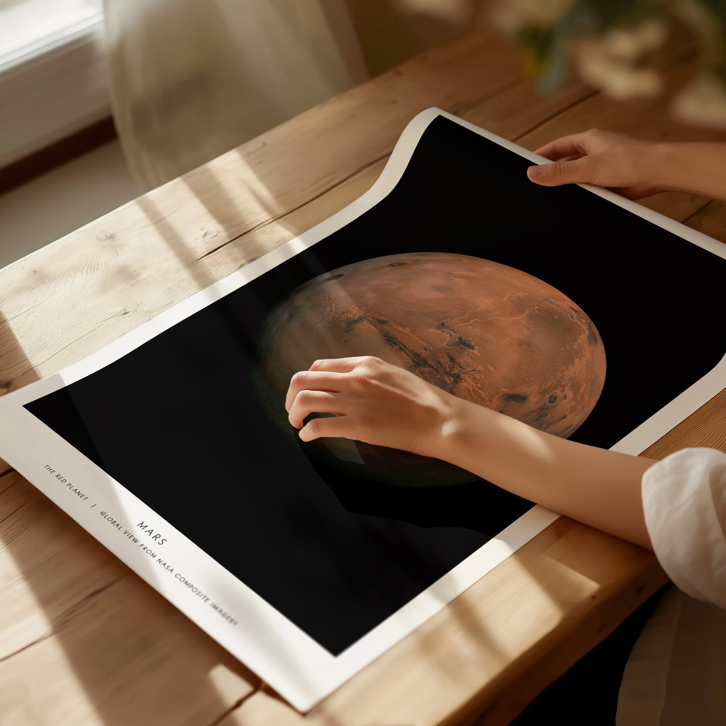 Person holding a poster with an image of Mars on a wooden table