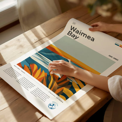 A person examines a colorful Waimea Bay poster on a wooden table, featuring abstract tropical foliage and wave patterns, with sunlight casting gentle shadows.