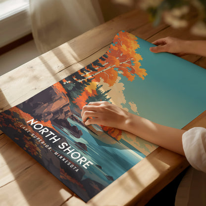 A person is holding a vibrant poster featuring the North Shore of Lake Superior, Minnesota, showcasing a colorful landscape with autumn foliage, evergreen trees, and a serene body of water.