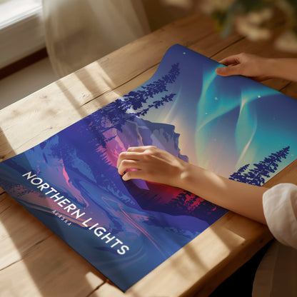 A person holding a colorful Northern Lights Alaska poster on a wooden table, featuring vibrant aurora borealis and silhouetted trees under a starry sky.