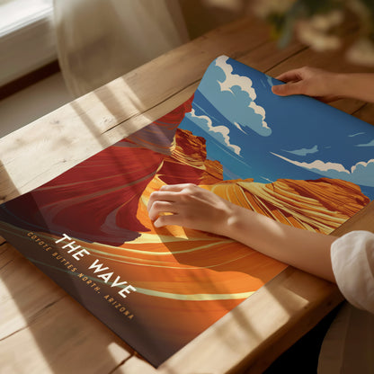 A person unrolls a vibrant poster of The Wave at Coyote Buttes, North Arizona, showcasing swirling sandstone formations under a blue sky with clouds. Sunlight streams across the table.