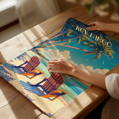 A person arranges a vibrant Key Largo poster featuring palm trees, Adirondack chairs, and a beach scene on a wooden table under warm.