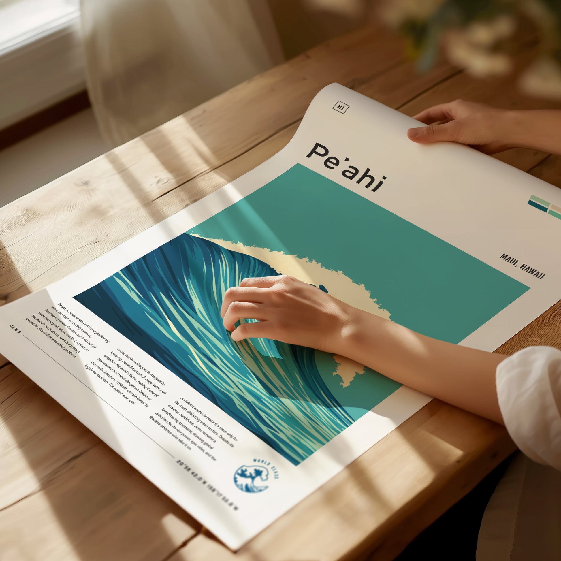 A person unrolls a Peʻahi Jaws Maui surf poster on a wooden table, showcasing a stylized wave design. Soft natural light illuminates the scene.