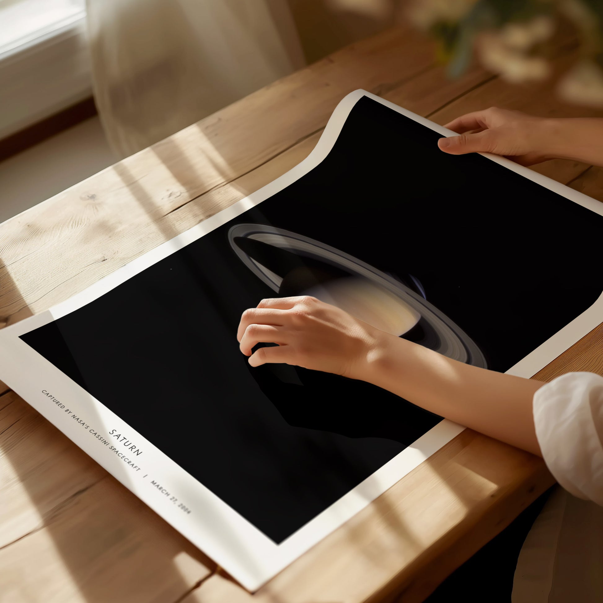 Person holding a large poster of Saturn on a wooden table