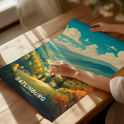 A person unrolls a colorful Gatlinburg, Tennessee poster depicting a vibrant landscape with lush forests and rolling hills.