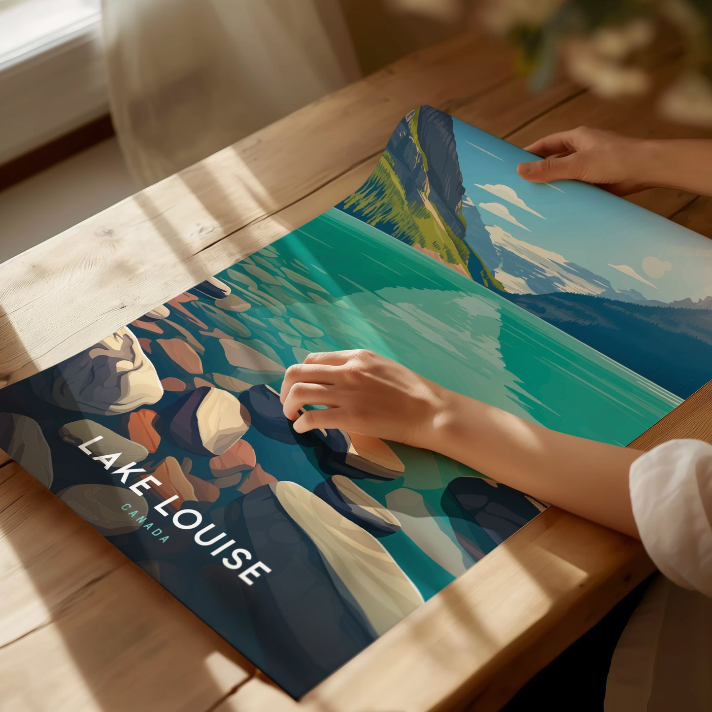 A person is holding a colorful Lake Louise poster with turquoise water and rocky shores, placed on a wooden table in natural sunlight. The text reads Lake Louise Canada.