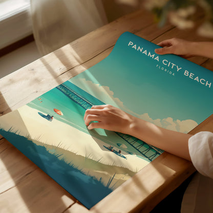 A person unrolls a vibrant Panama City Beach poster on a wooden table, featuring turquoise waters, a sandy beach, and a pier under a sunny sky.