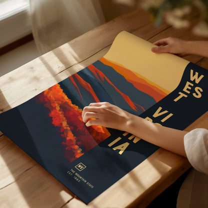 A person rolls out a colorful West Virginia poster on a wooden table, featuring vibrant red and blue abstract mountain designs with text on the side.