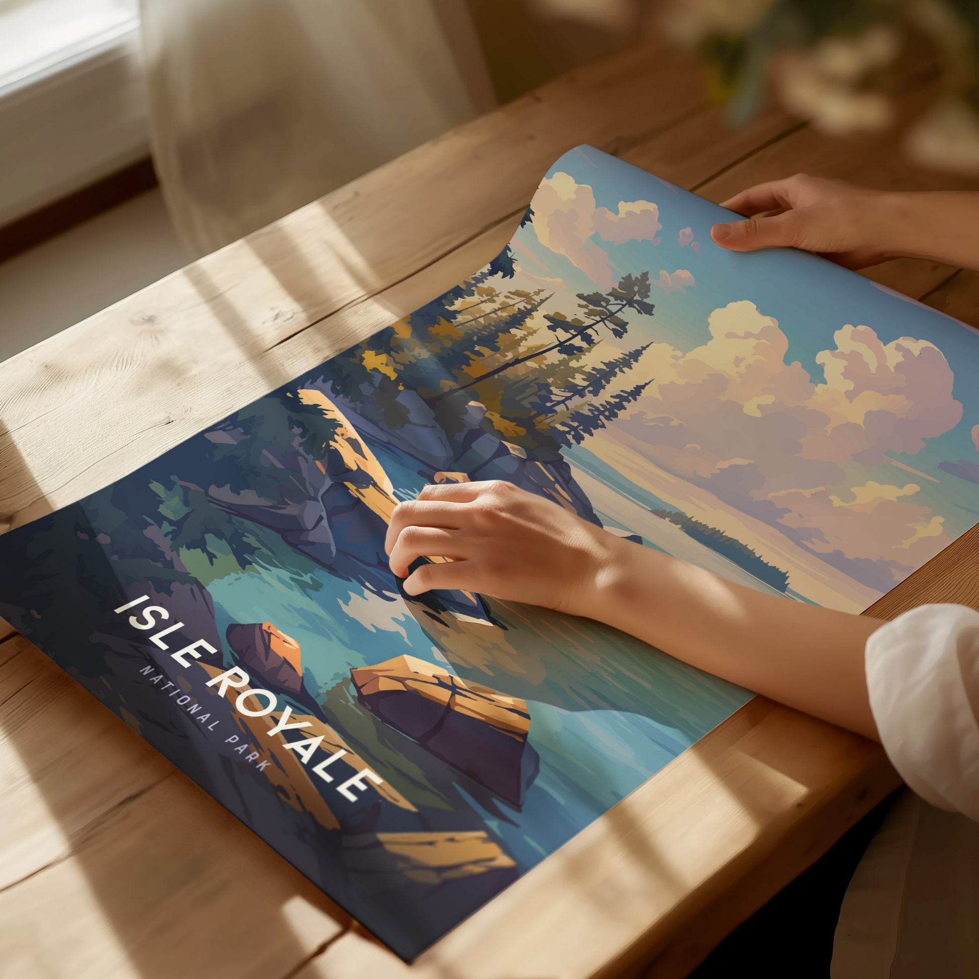 A person unrolls an Isle Royale National Park poster on a wooden table, featuring colorful illustrations of rocky shorelines and pine trees under a vibrant sky.