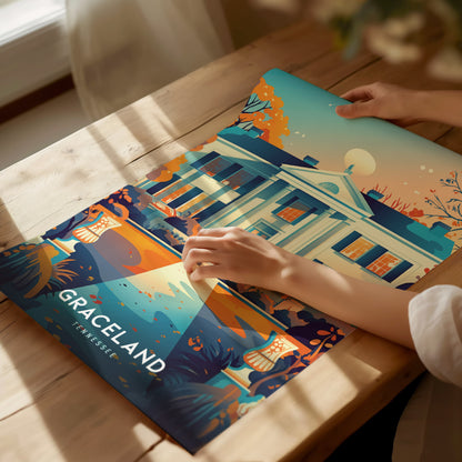 A person is holding a colorful poster of Graceland, featuring an artistic depiction of the iconic mansion with vibrant trees and a clear sky. Sunlight streams onto the wooden table.