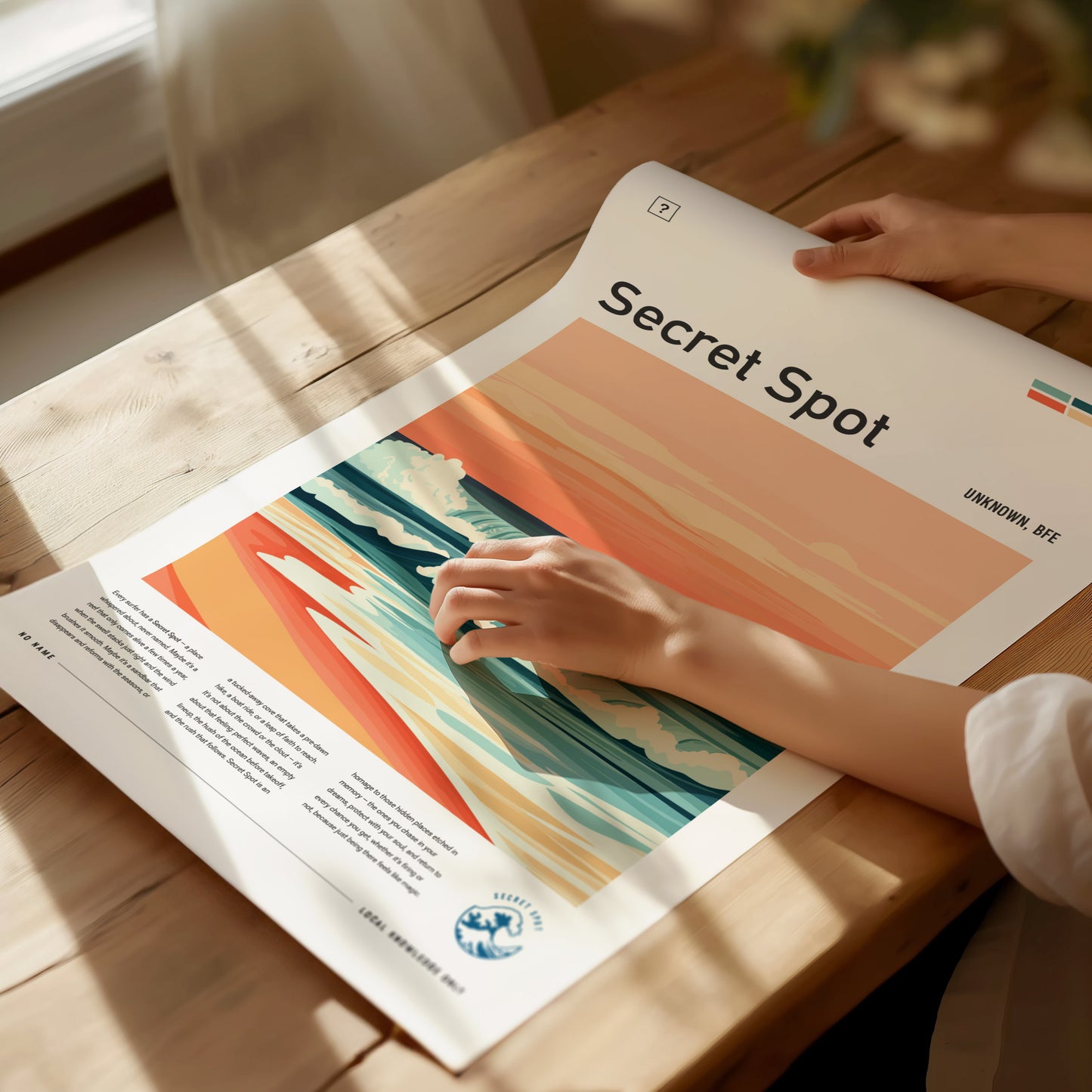 A person is holding a Secret Spot surf poster featuring colorful waves and a sunset design on a wooden table. Sunlight casts soft shadows across the scene.