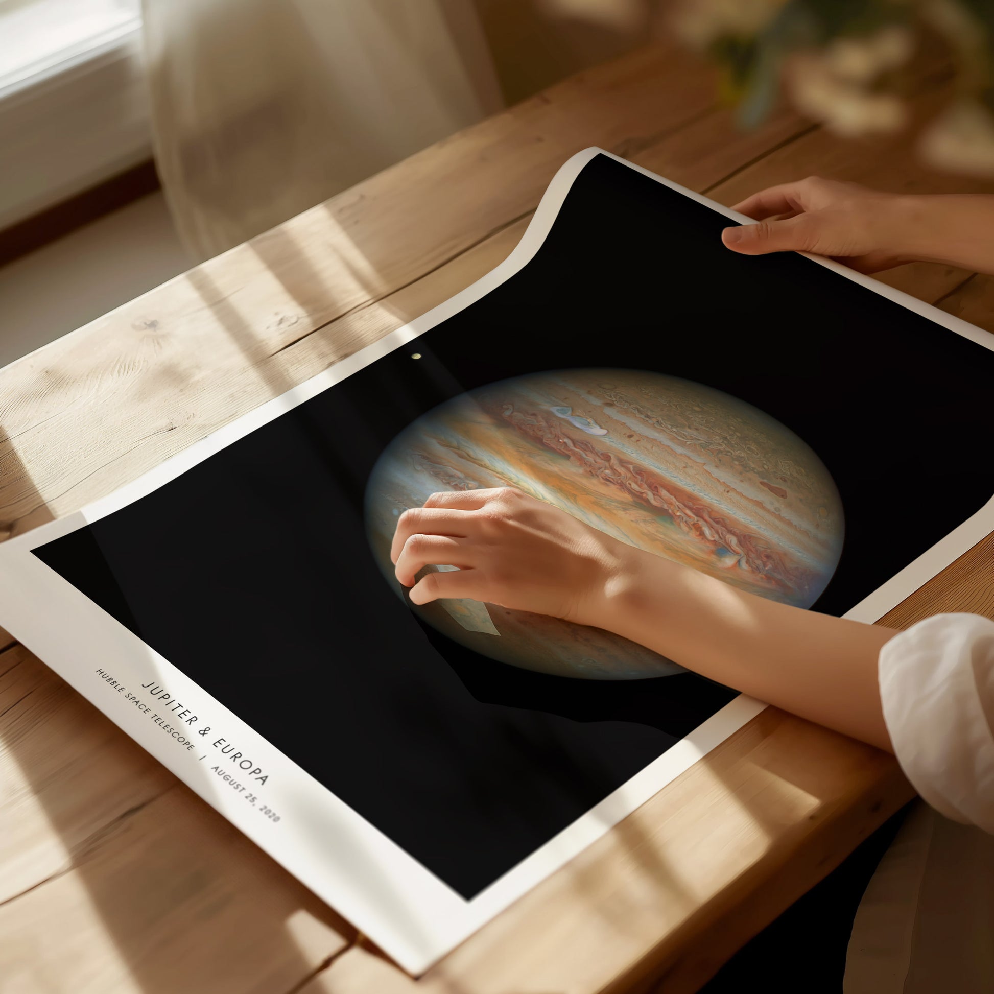 Person holding a poster with an image of Jupiter on a wooden table
