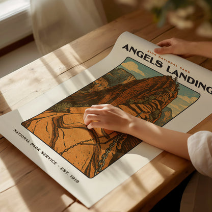 A person carefully unrolls an Angels Landing poster on a wooden table, showcasing a vintage-style illustration of the iconic sandstone cliffs in Zion National Park.