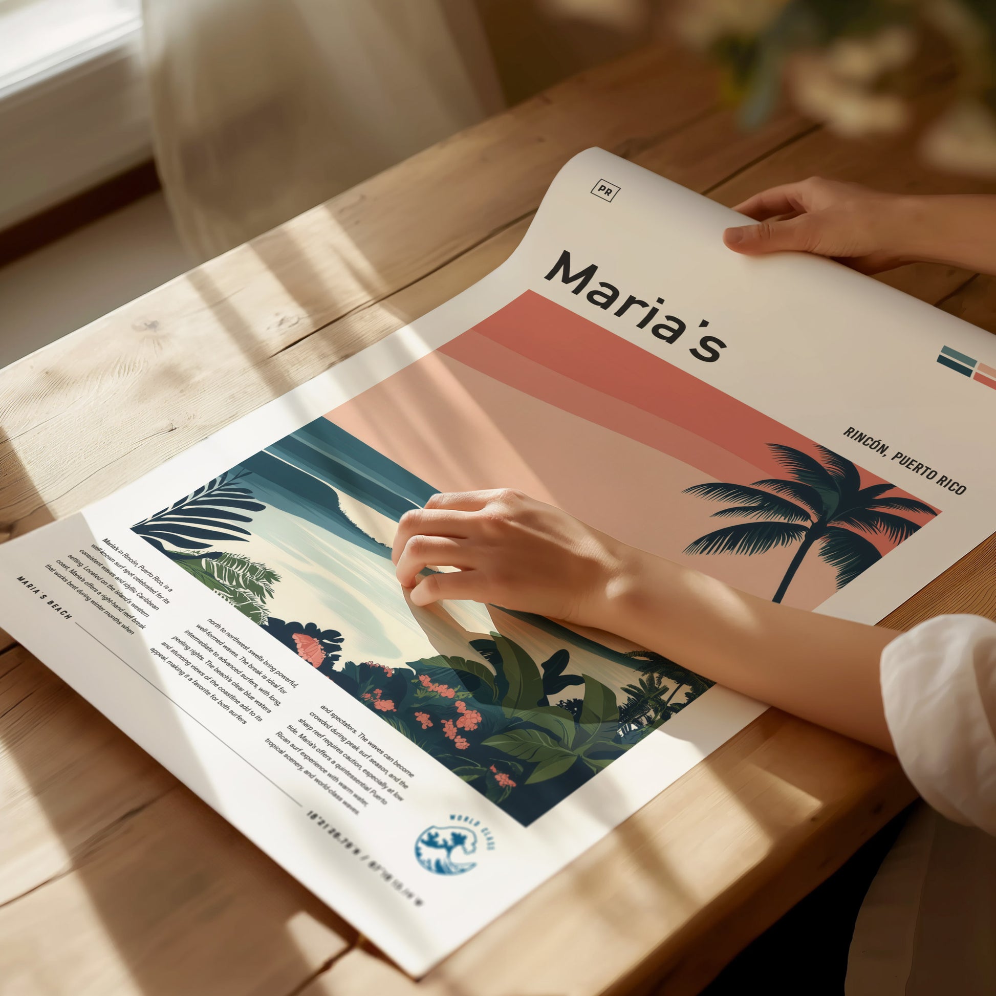A person gently handles a vibrant surf art poster titled Marias, featuring tropical plants and palm trees, with text indicating Rincon, Puerto Rico, on a sunlit wooden table.