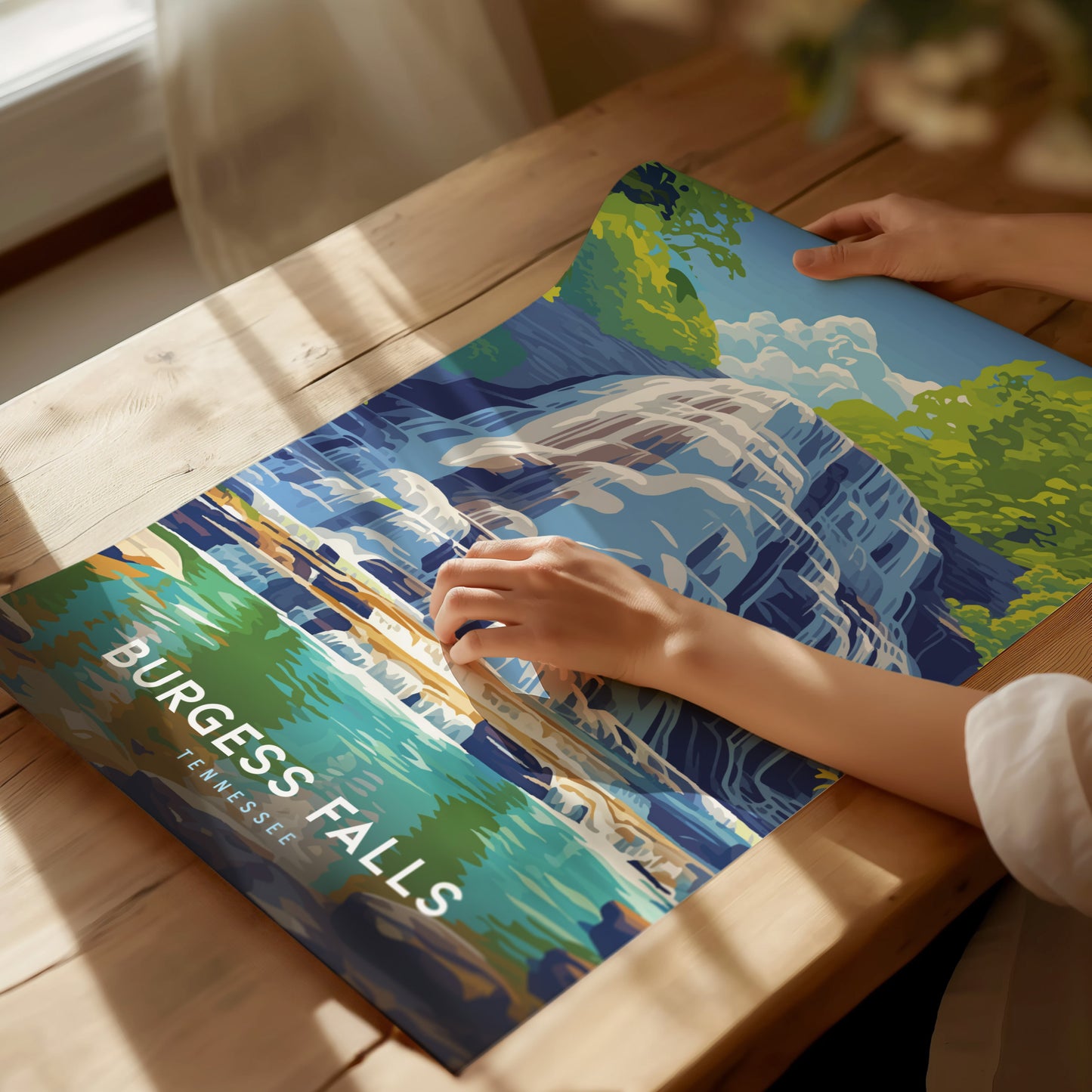 A person holds a colorful poster depicting Burgess Falls with cascading water and lush greenery, placed on a sunlit wooden table. The text reads Burgess Falls, Tennessee.