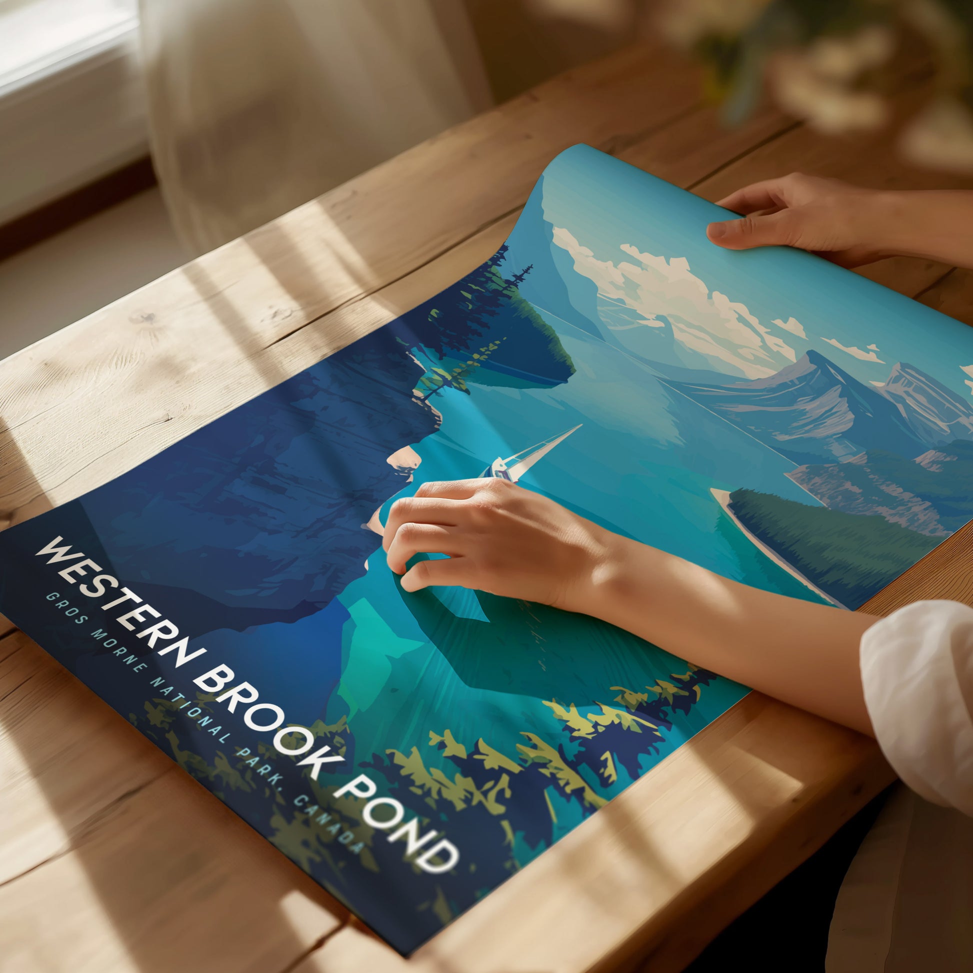 A person gently unrolls a vibrant Western Brook Pond poster on a wooden table, showcasing a scenic fjord with towering cliffs and clear waters. Sunlight filters through a nearby window.
