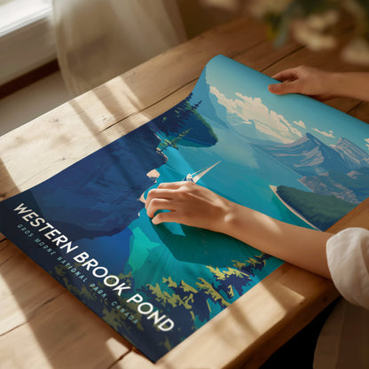 A person gently unrolls a vibrant Western Brook Pond poster on a wooden table, showcasing a scenic fjord with towering cliffs and clear waters. Sunlight filters through a nearby window.