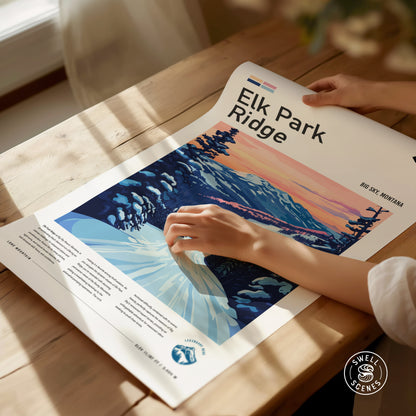 A person holds an Elk Park Ridge poster on a wooden table, showcasing a stylized mountain landscape with a colorful sky. Sunlight casts gentle shadows across the scene.
