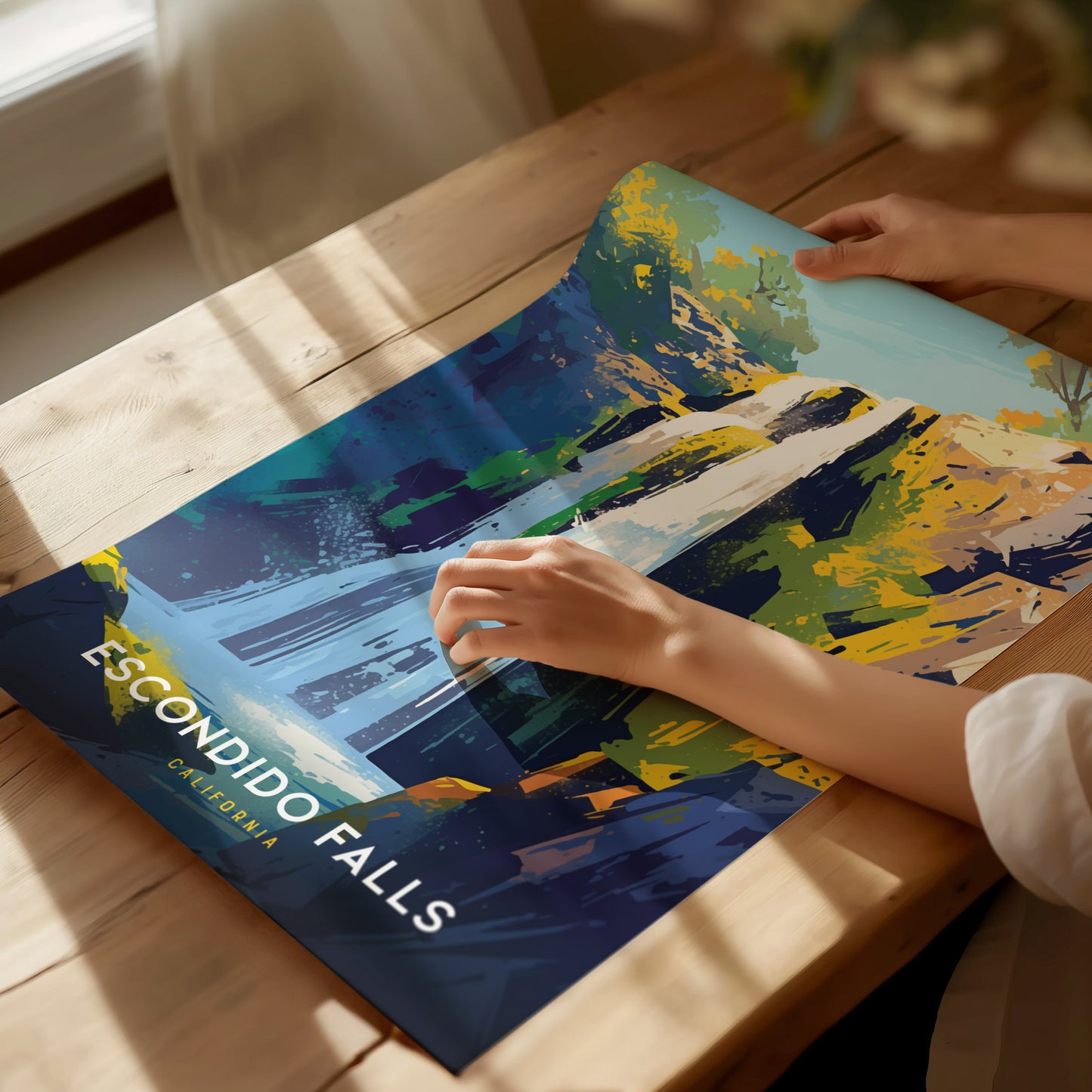 A person holds a vibrant, colorful poster of Escondido Falls on a wooden table. The artwork features abstract, bold strokes in blues, greens, and yellows, capturing the waterfalls essence.