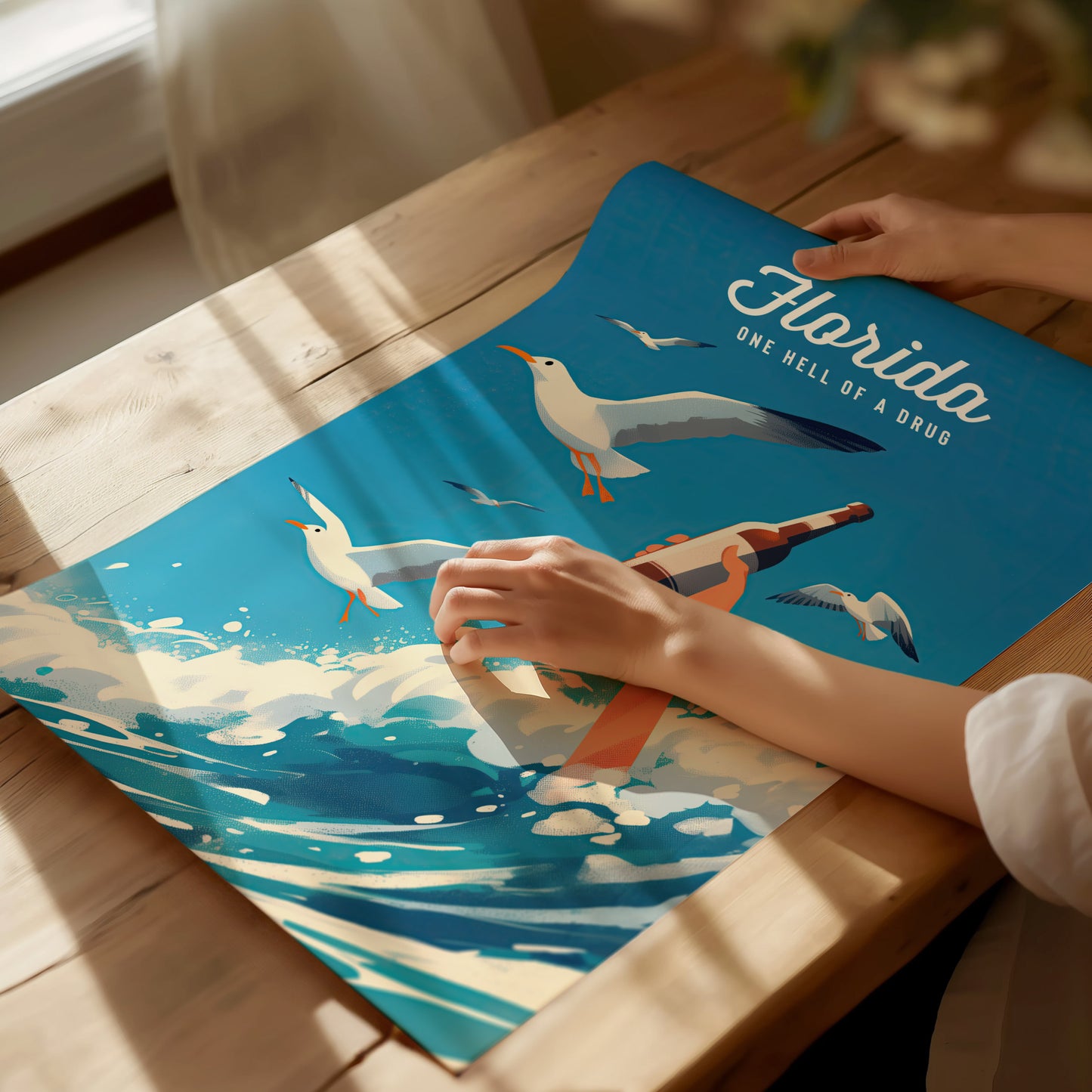 A person unrolls a vibrant poster depicting seagulls, waves, and a hand holding a bottle, with the text Florida One Hell Of A Drug against a blue background.