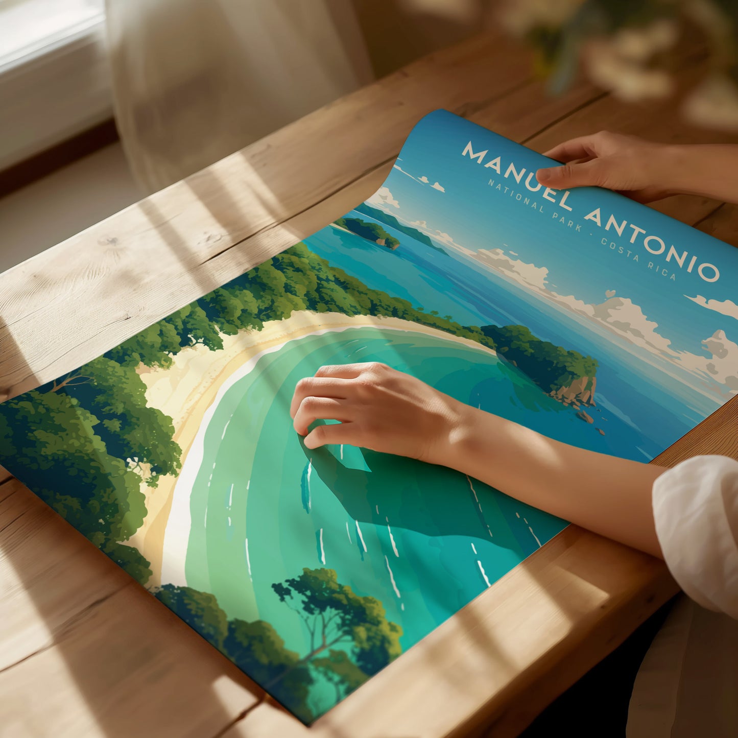 A person places a hand on a vibrant poster of Manuel Antonio National Park, showcasing a scenic coastline with lush greenery and turquoise waters, on a wooden table.