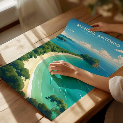 A person places a hand on a vibrant poster of Manuel Antonio National Park, showcasing a scenic coastline with lush greenery and turquoise waters, on a wooden table.