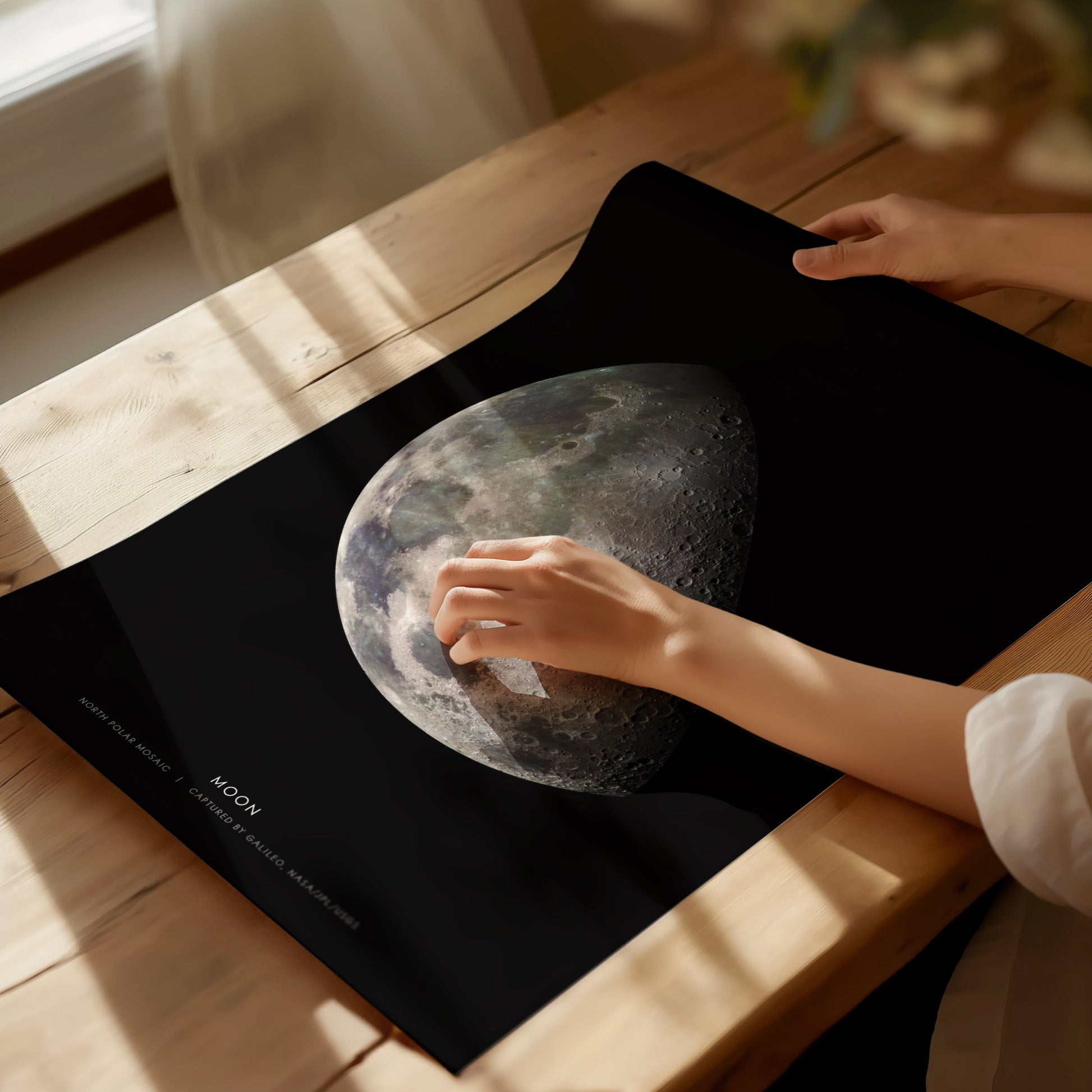 Person holding a poster of the moon on a wooden table