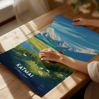 A person unrolls a colorful Katmai National Park poster depicting a scenic landscape with mountains and greenery.