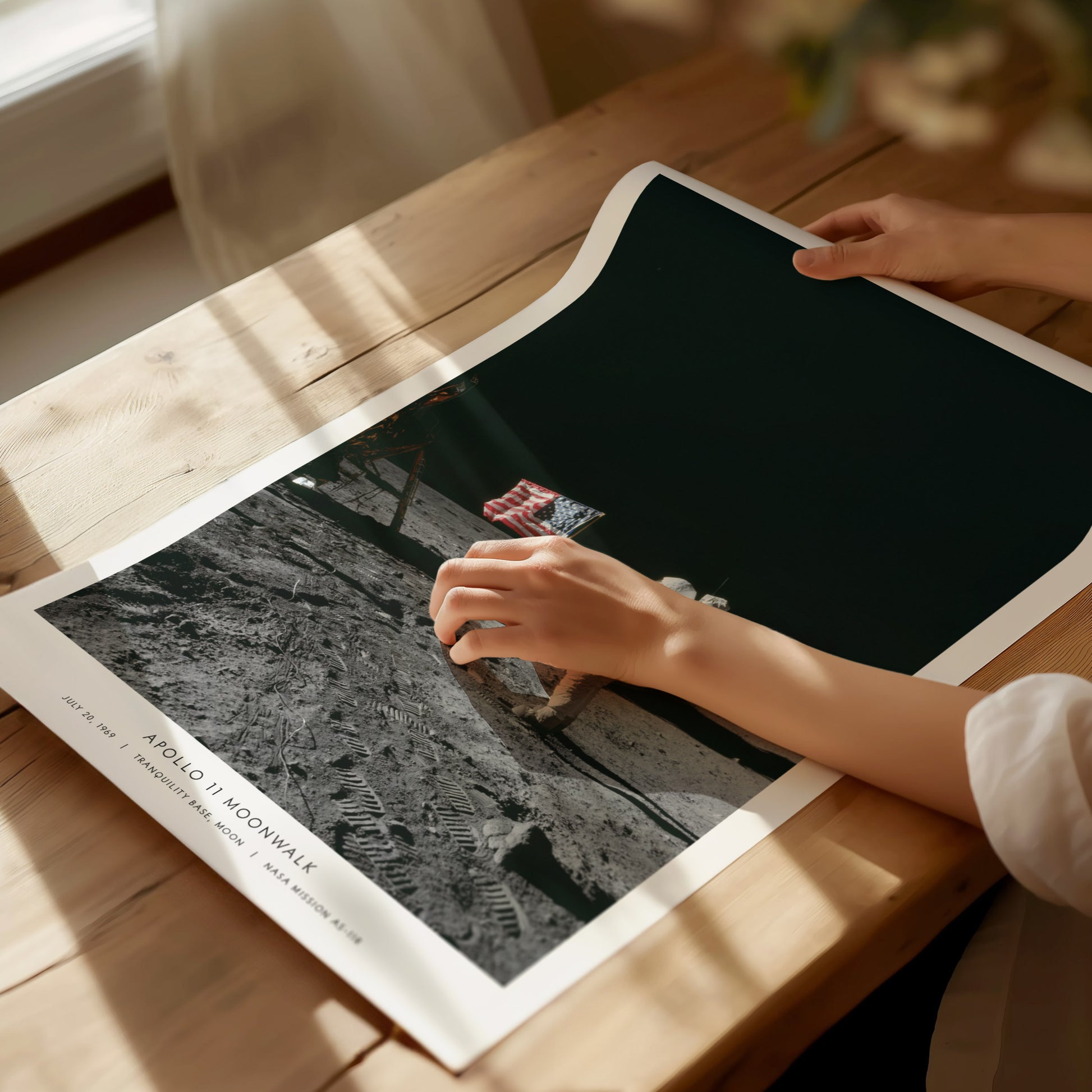 Person holding a poster with a black and white photo of Apollo 11 Buzz Aldrin on a wooden table.