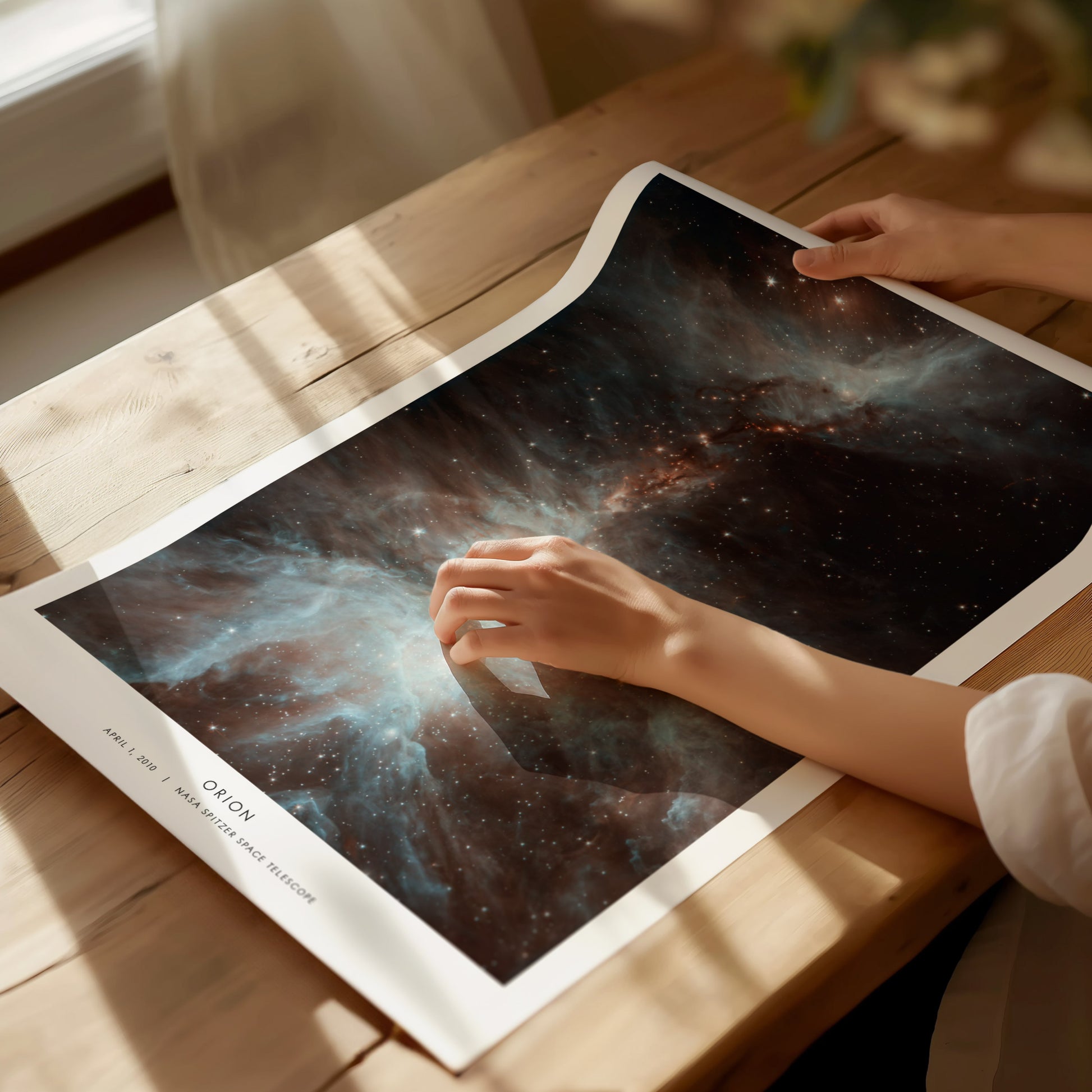 Person holding a Orion space-themed poster on a wooden table