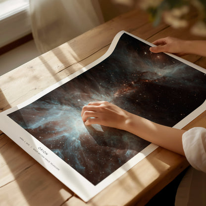 Person holding a Orion space-themed poster on a wooden table
