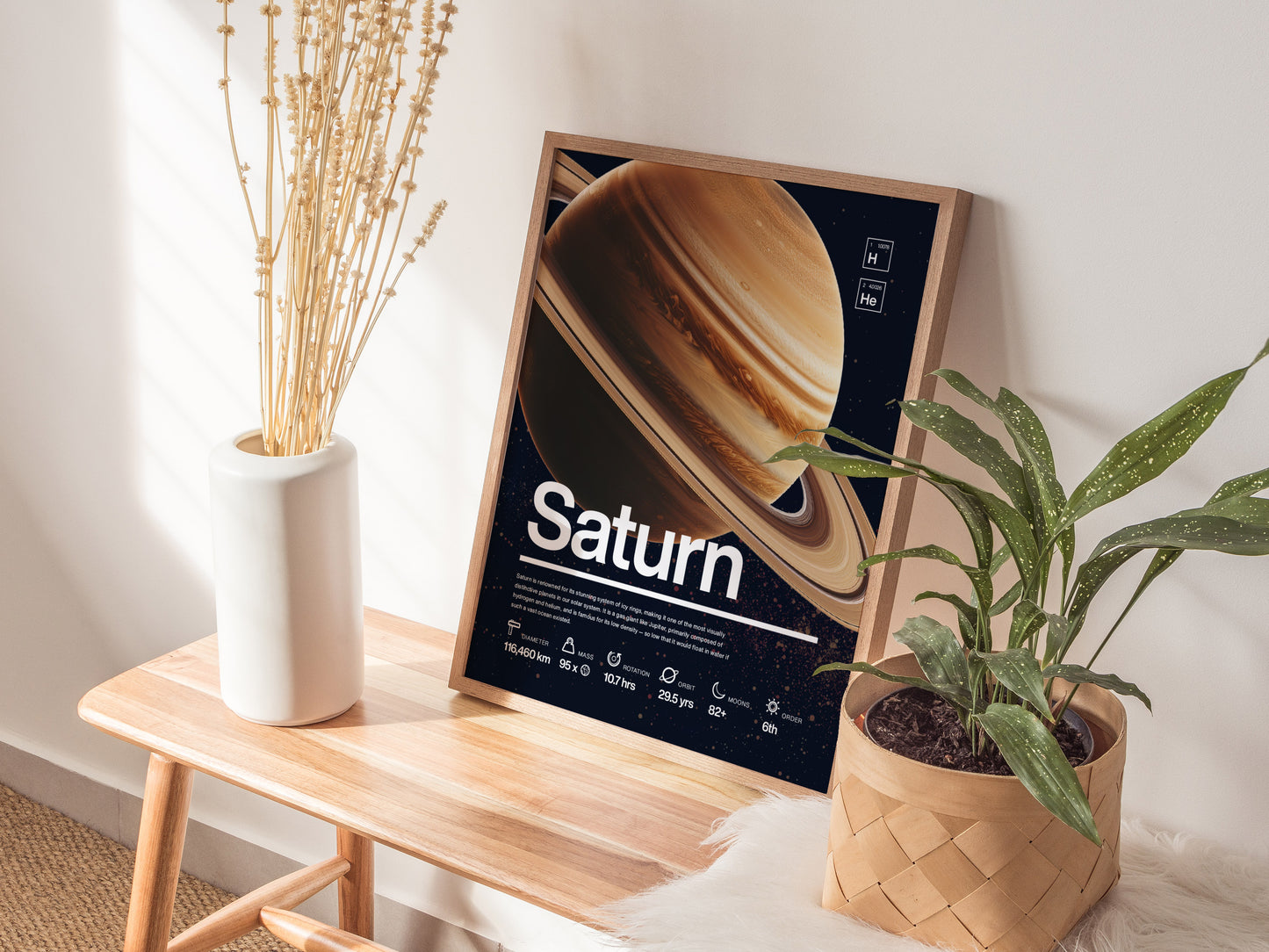 A framed Saturn poster rests on a wooden bench beside a white vase with dried flowers and a potted green plant, creating a cozy, educational display.