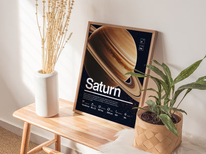A framed Saturn poster rests on a wooden bench beside a white vase with dried flowers and a potted green plant, creating a cozy, educational display.