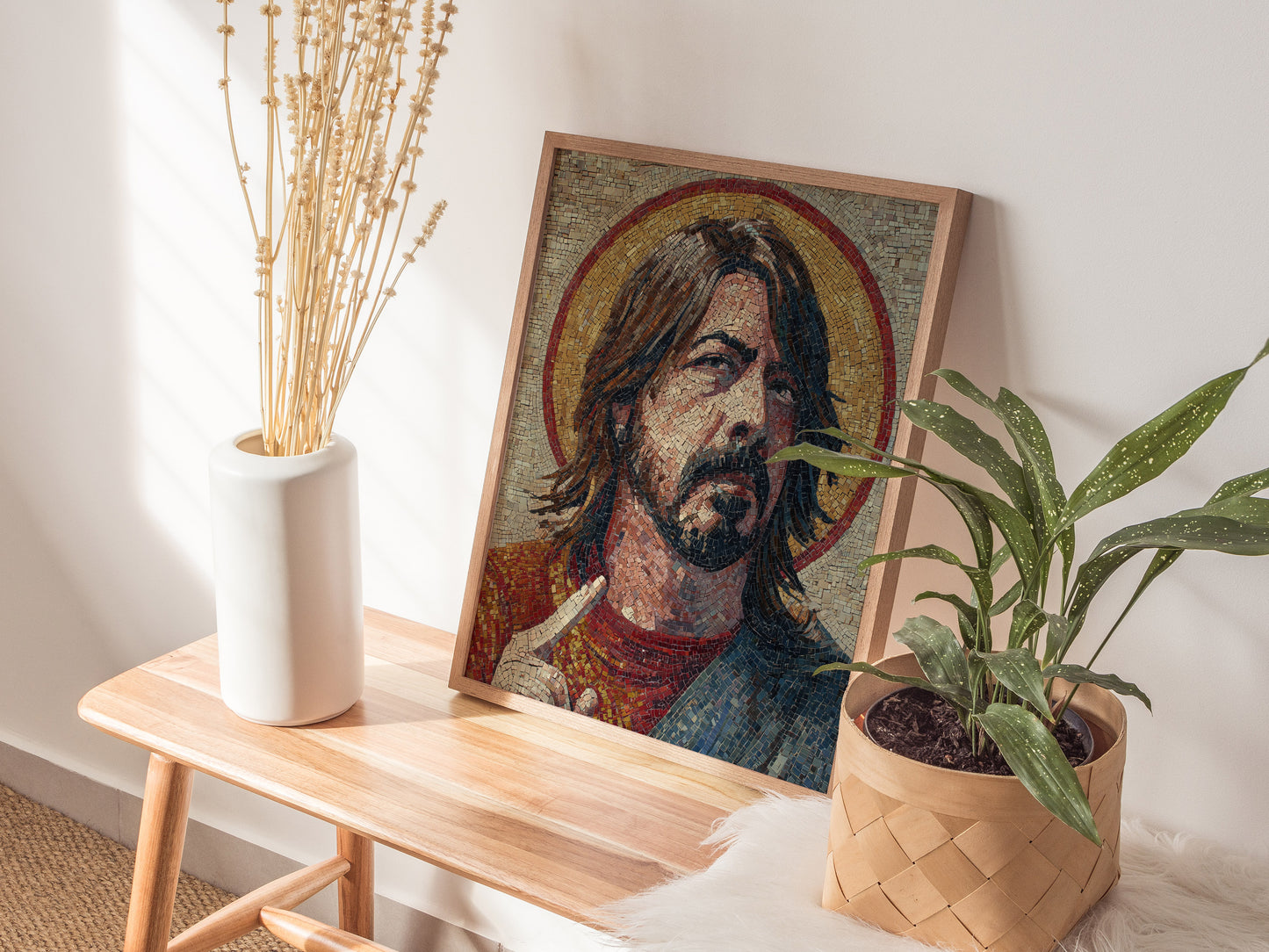 A beautifully framed mosaic art piece depicting a man with long hair and a beard, styled in a Byzantine religious iconography. The artwork is displayed on a wooden table alongside a white vase with dried flowers and a potted plant.