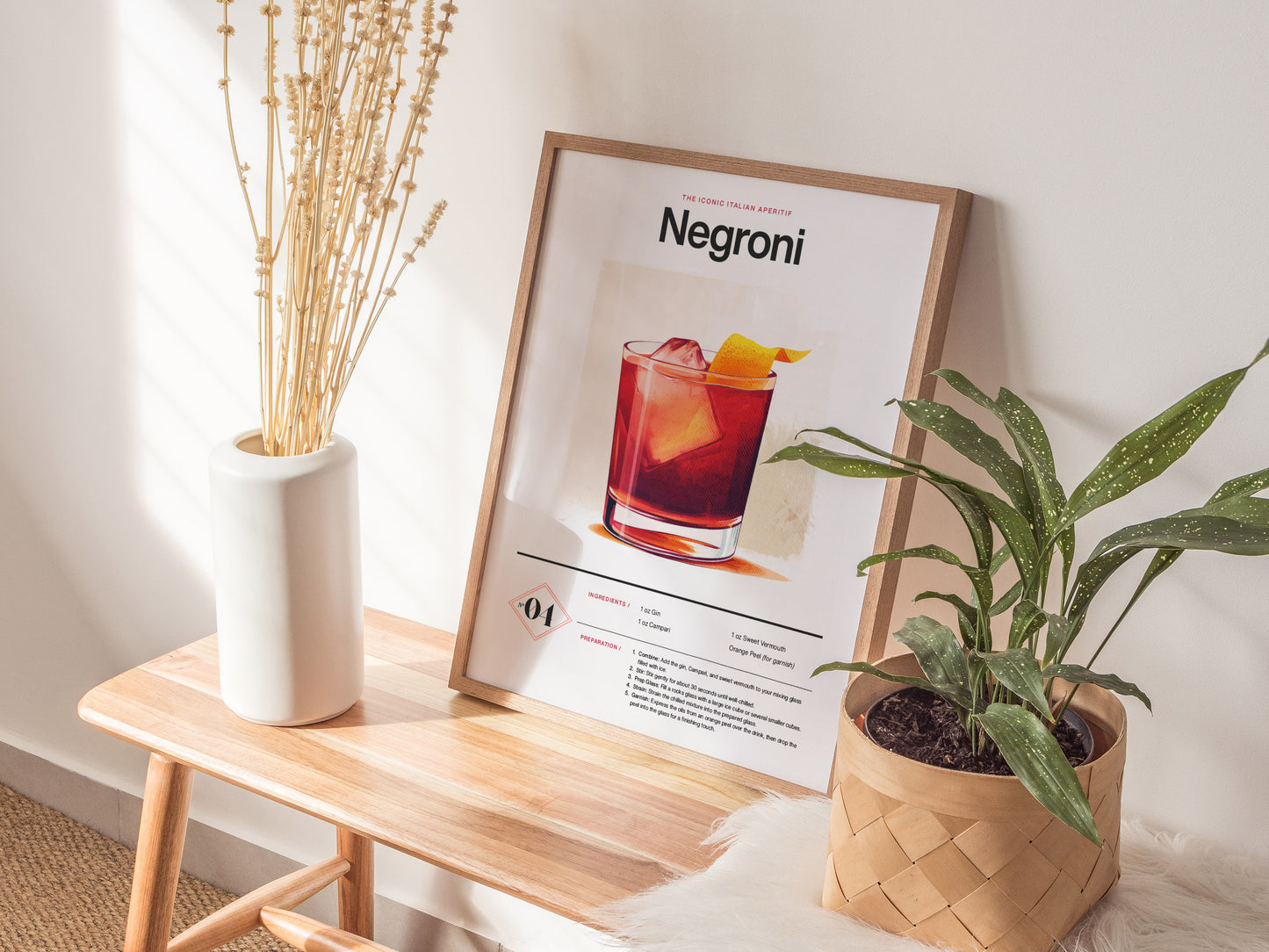 A Negroni cocktail poster rests on a wooden bench between a white vase with dried flowers and a potted plant. Sunlight casts soft shadows across the scene.