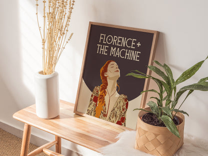 A Florence + The Machine poster rests on a wooden table between a white vase with dried plants and a woven basket with a green plant.